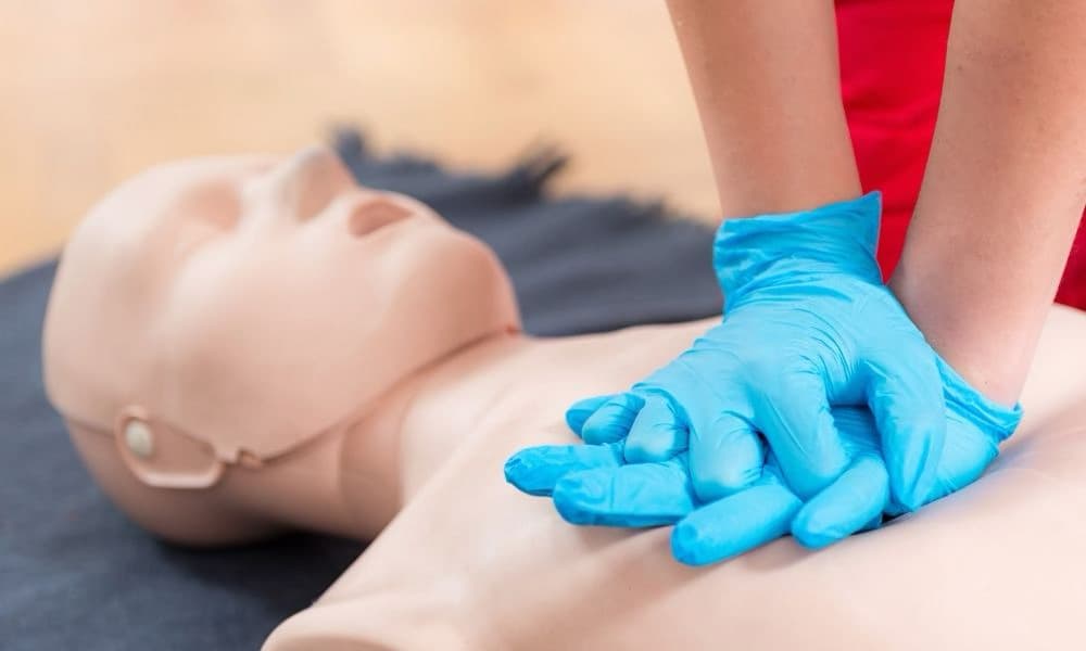 Gloved hands practicing chest compressions on a CPR manikin