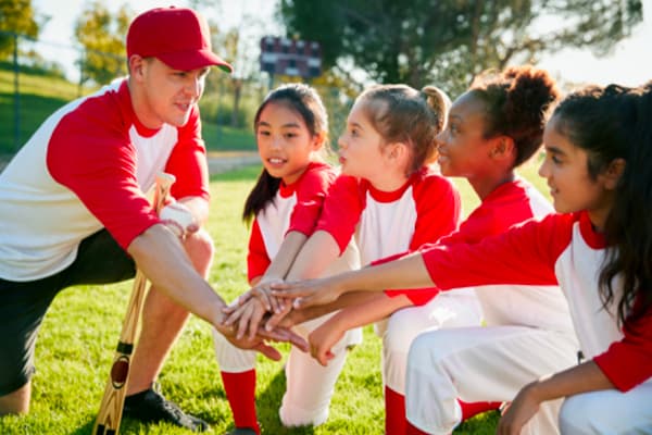 A youth baseball coach and players joining hands in a team huddle